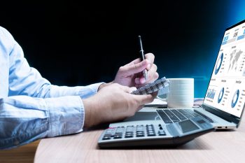 Persona revisando reportes financieros y gráficos contables en computador portátil, con calculadora y cuaderno, representando la integración contable automatizada a partir de la factura electrónica.